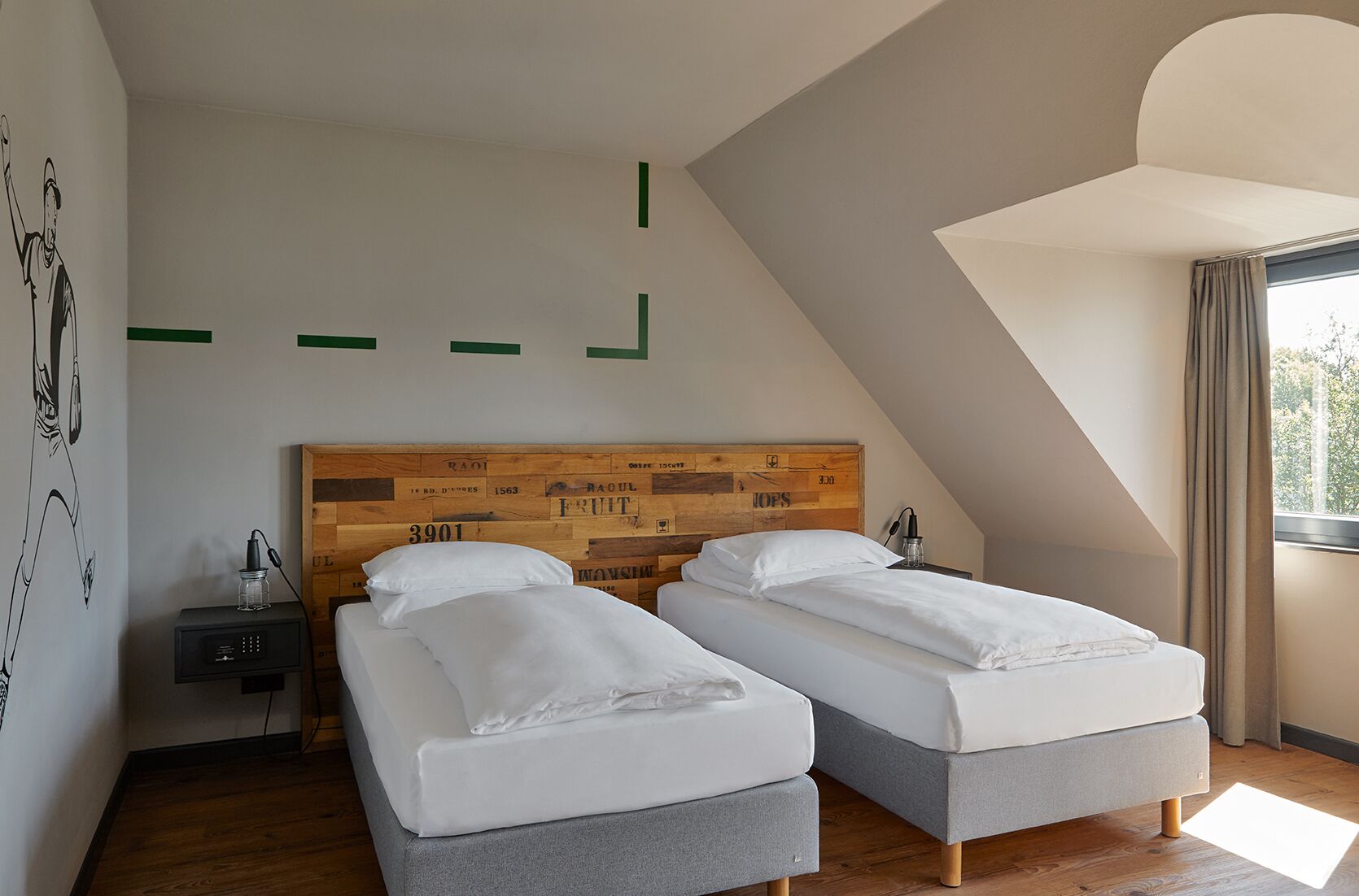 Une chambre avec deux lits simples, une tête de lit en bois ornée de chiffres, une table de chevet et un mur décoré d’œuvres d’art abstraites.