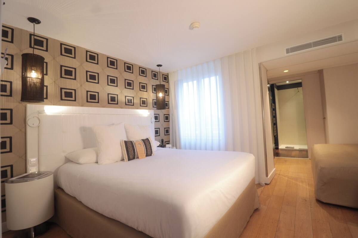 Een hotelkamer met een groot bed, nachtkastje, lamp en stoel.