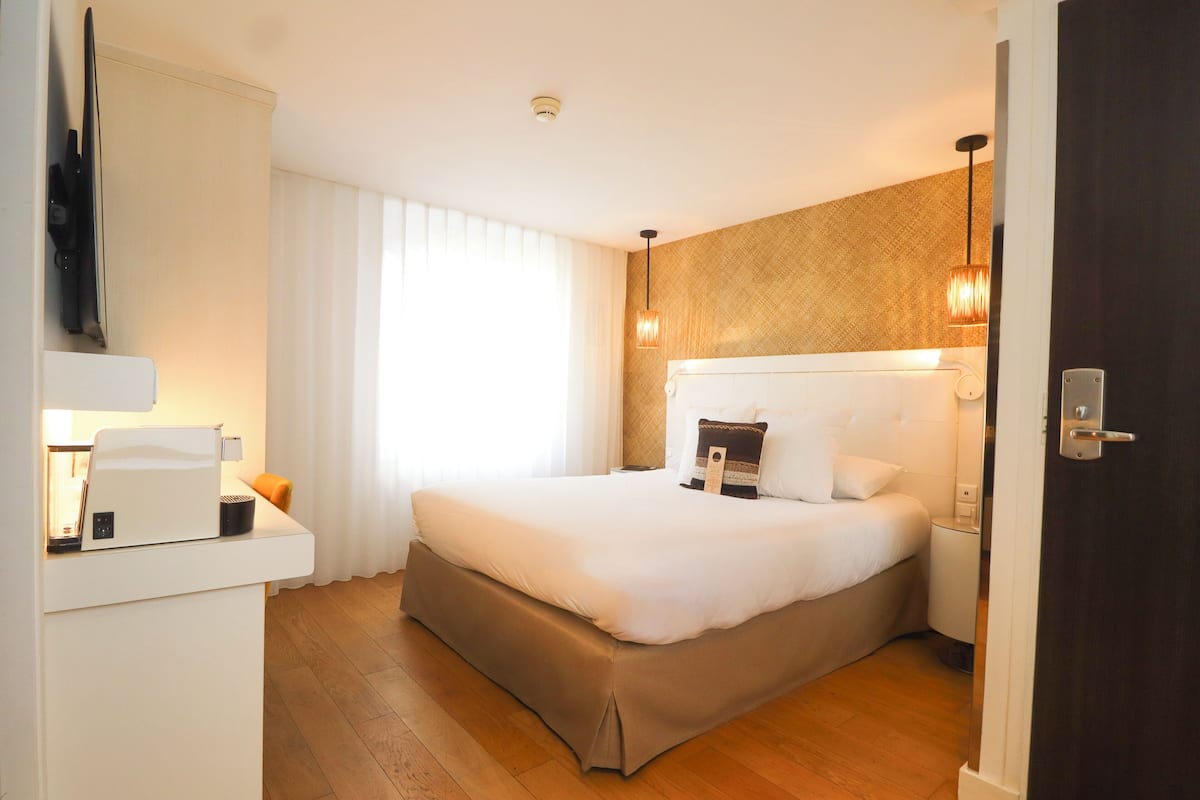 Een hotelkamer met een bed, een bureau met lamp, een televisie en een raam met gordijnen.