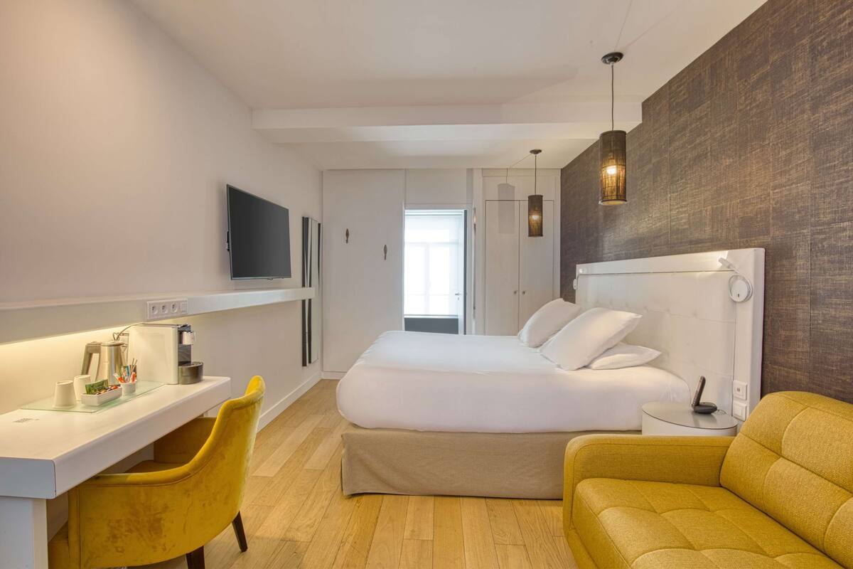 Een moderne hotelkamer met een bed, een bureau, een gele stoel en een bank.