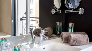 Een moderne badkamer met een groot wit wastafelmeubel, twee spiegels en een raam met uitzicht op gebouwen.