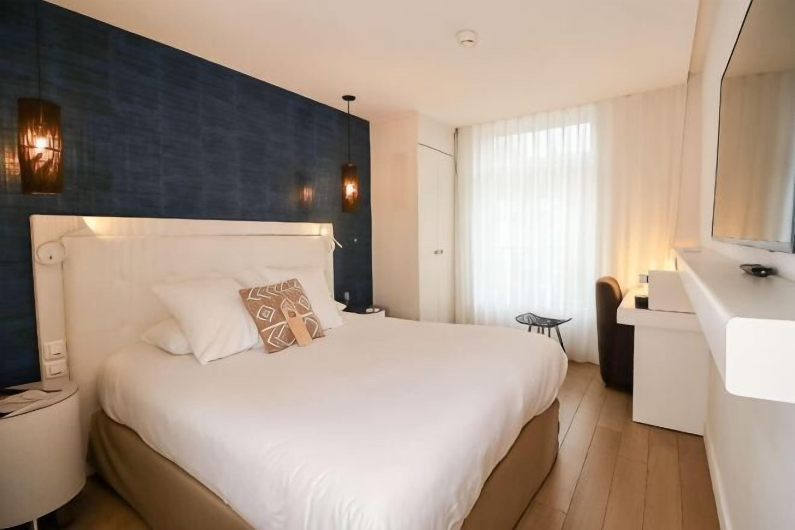 Ein Hotelzimmer mit einem großen Bett, einem Schreibtisch, einem Sessel, einem Fernseher und einer Wandleuchte.