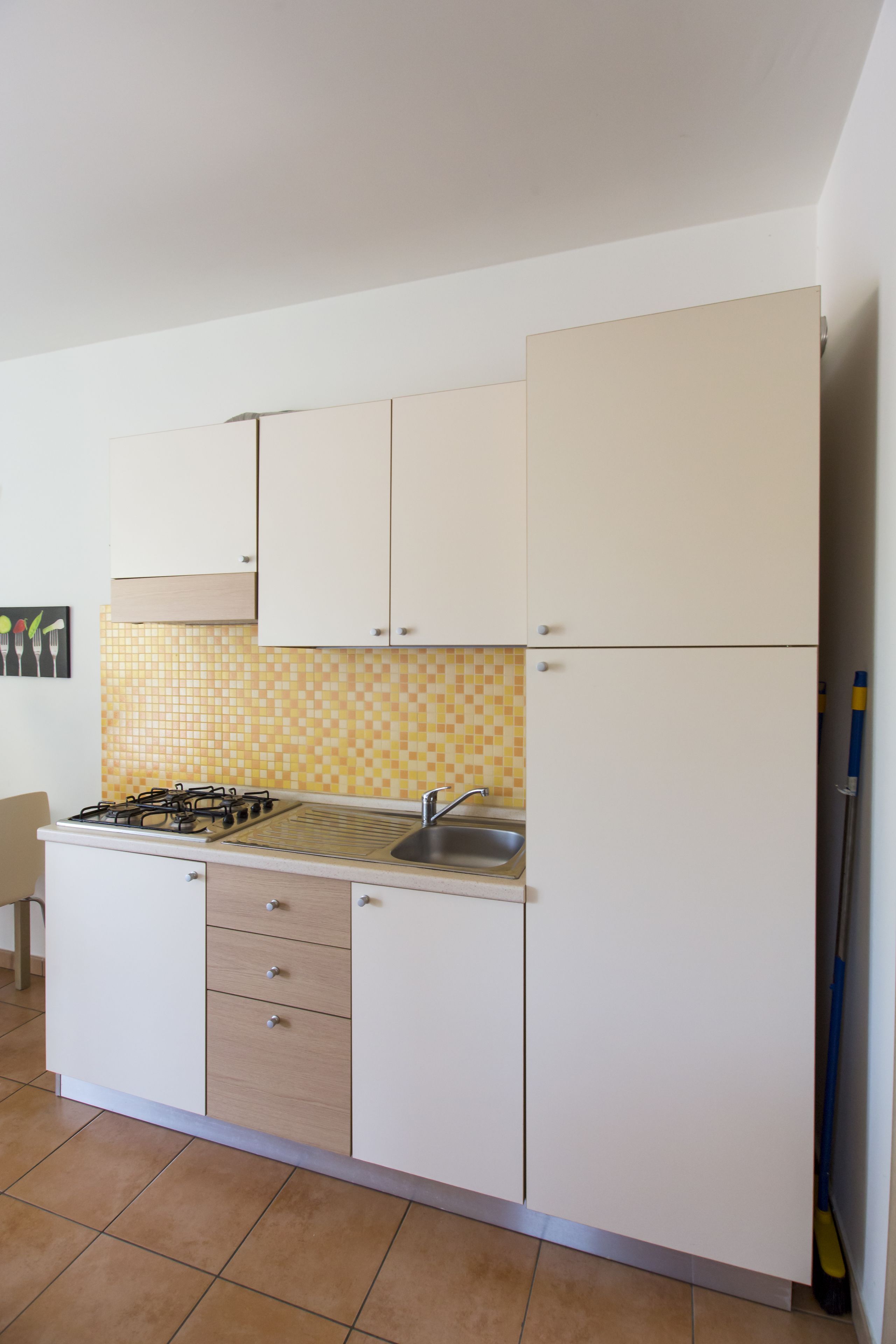 Une cuisine de taille réduite avec des meubles blancs, un plan de travail carrelé, une cuisinière à gaz et un évier.