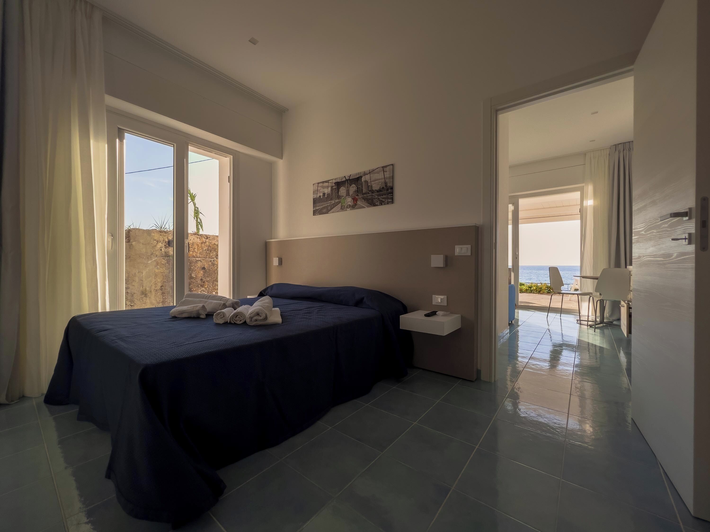 Quarto com duas camas, uma mesa de cabeceira, um quadro e vista para o mar.
