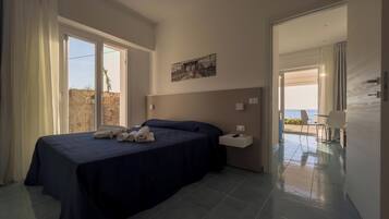 Quarto com duas camas, uma mesa de cabeceira, um quadro e vista para o mar.