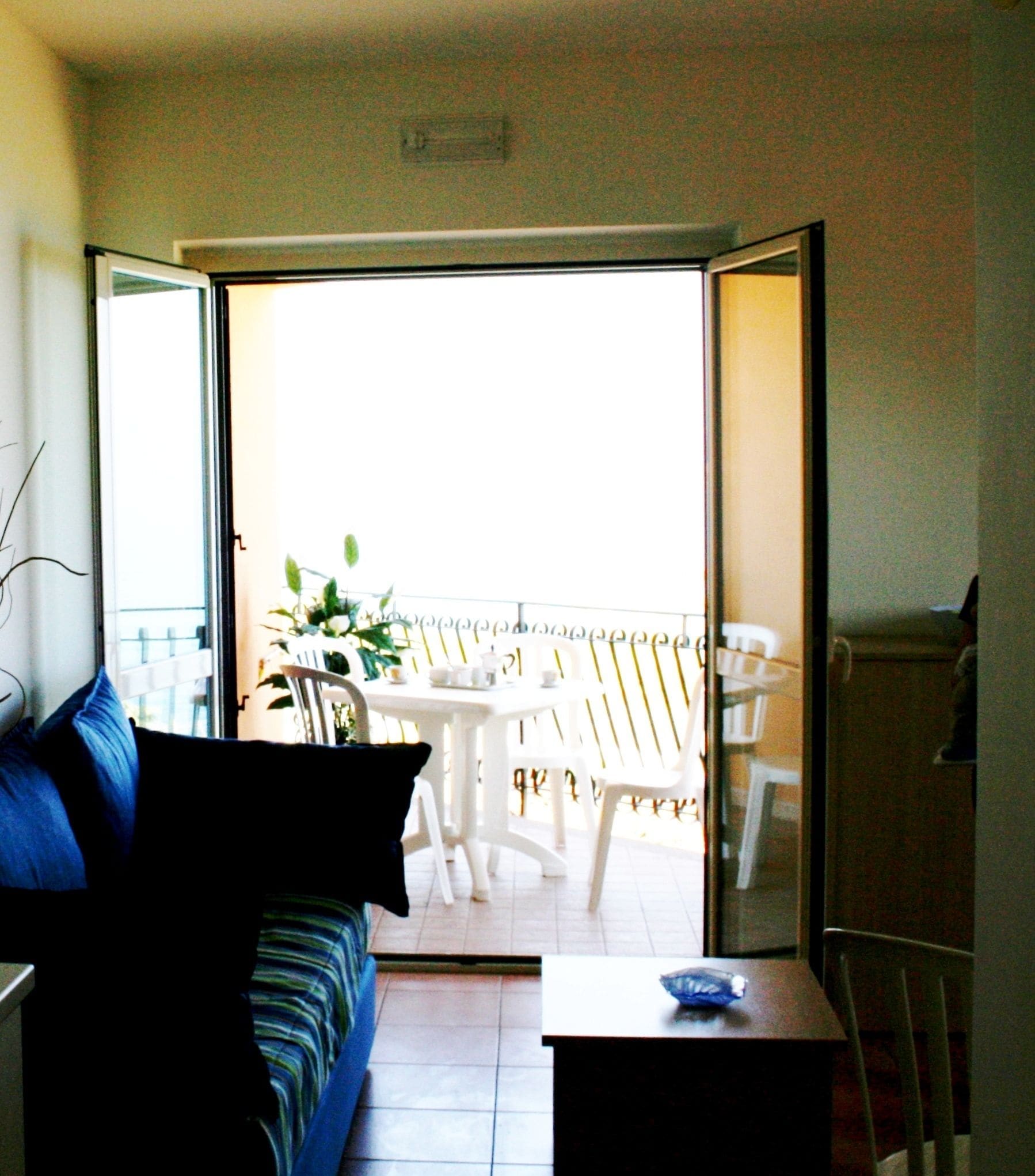 A room with a sofa, a small table, and a balcony with a table and chairs.