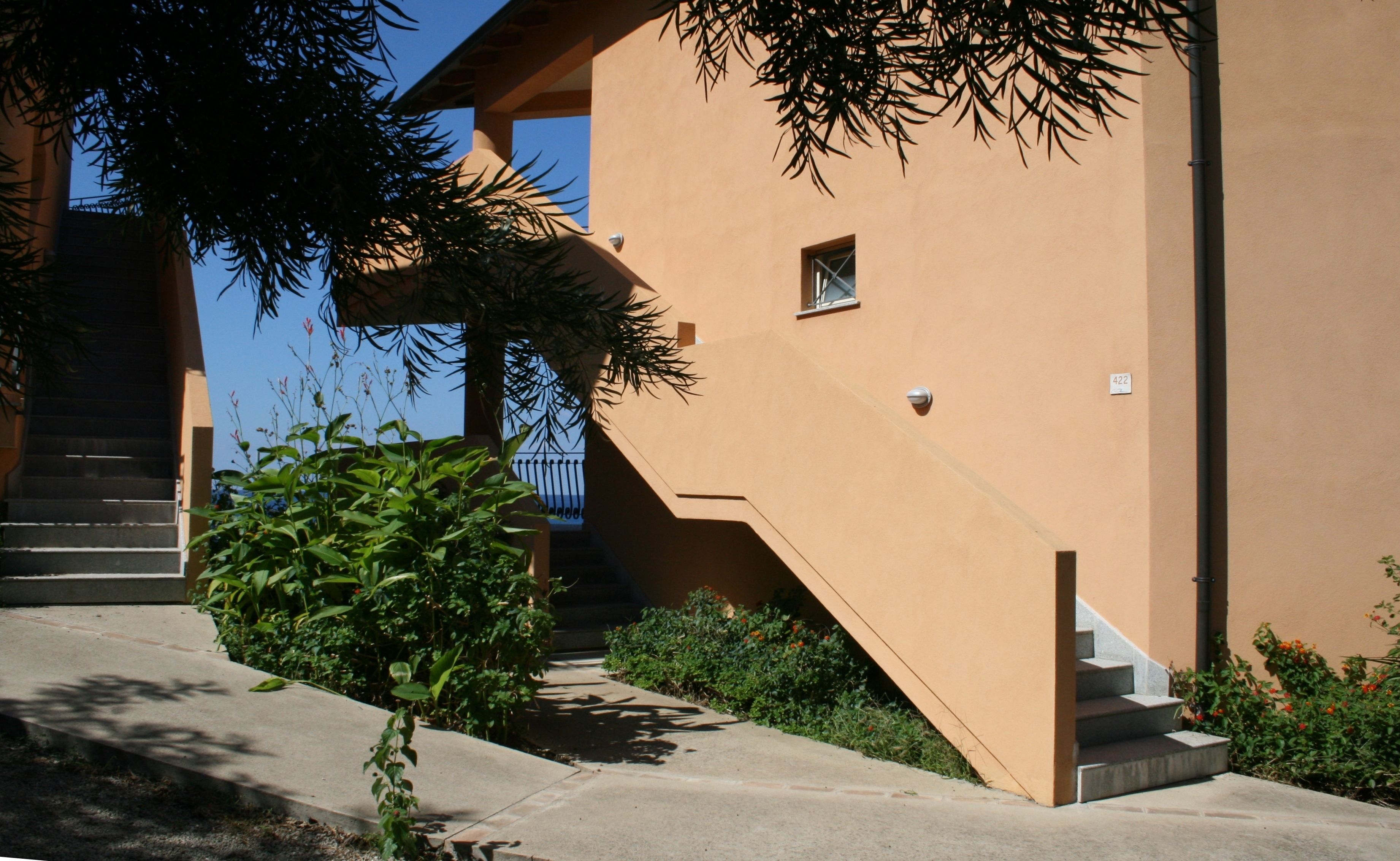 Un edificio de fachada color crema, con una escalera que lleva a un nivel superior y una ventana pequeña.