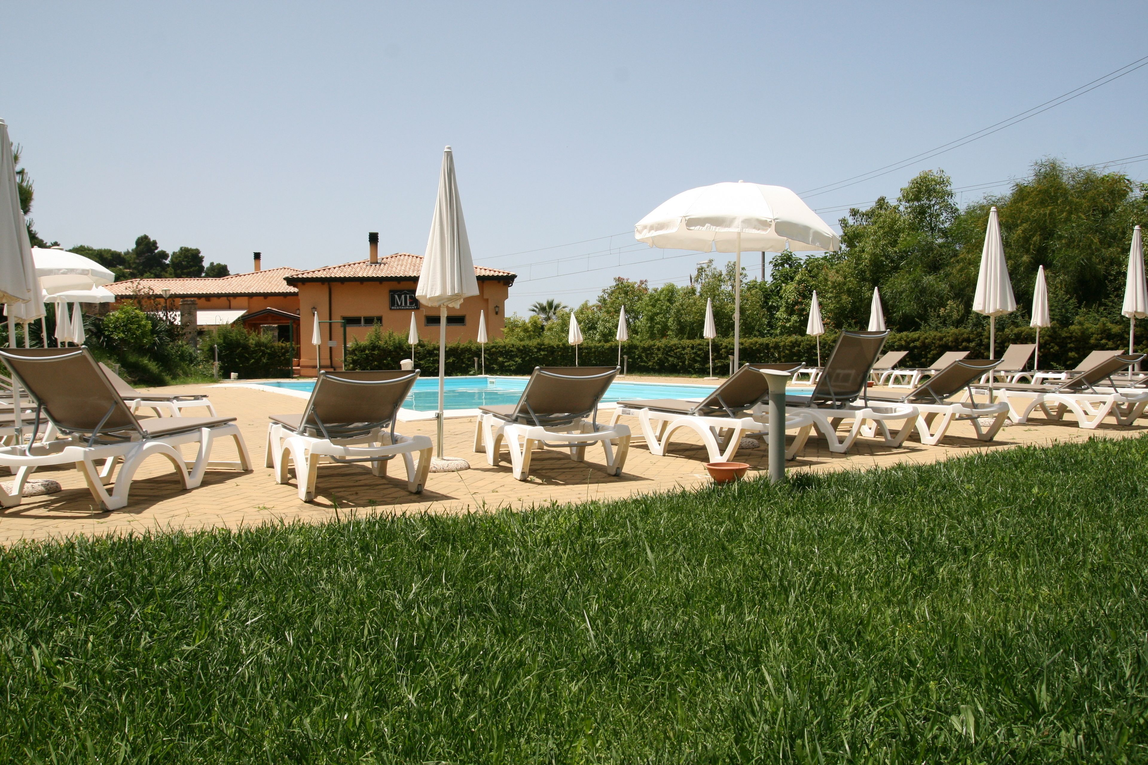 A poolside area with lounge chairs and umbrellas, a clear blue pool, and a building in the background.