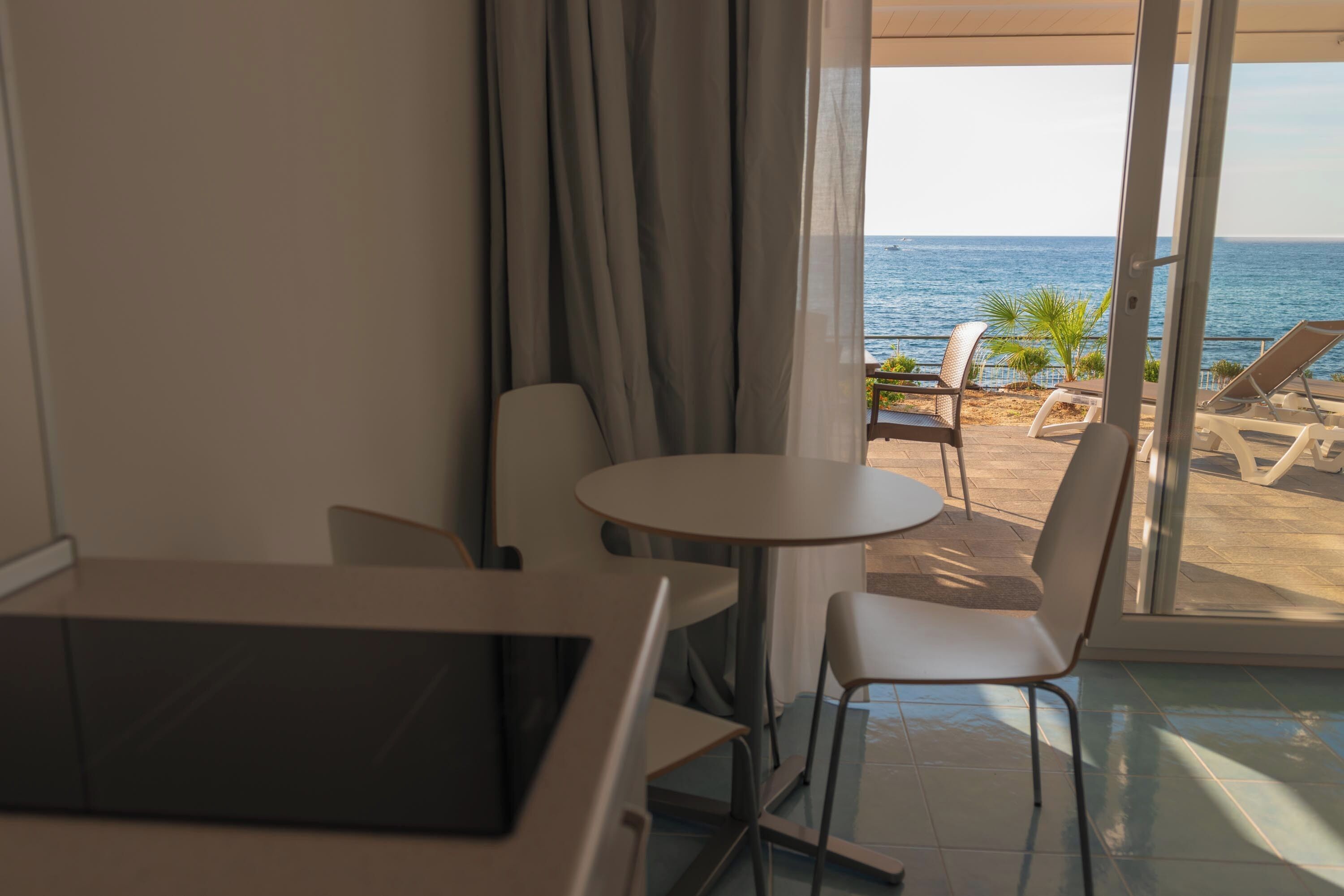 A hotel room with a view of the sea, a round table, and two chairs.