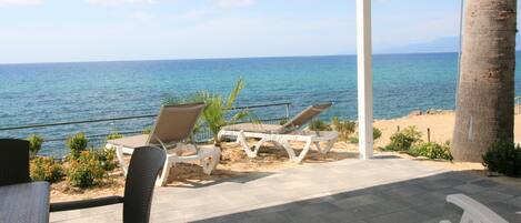 A covered outdoor seating area with chairs and tables, overlooking a beach and the sea.