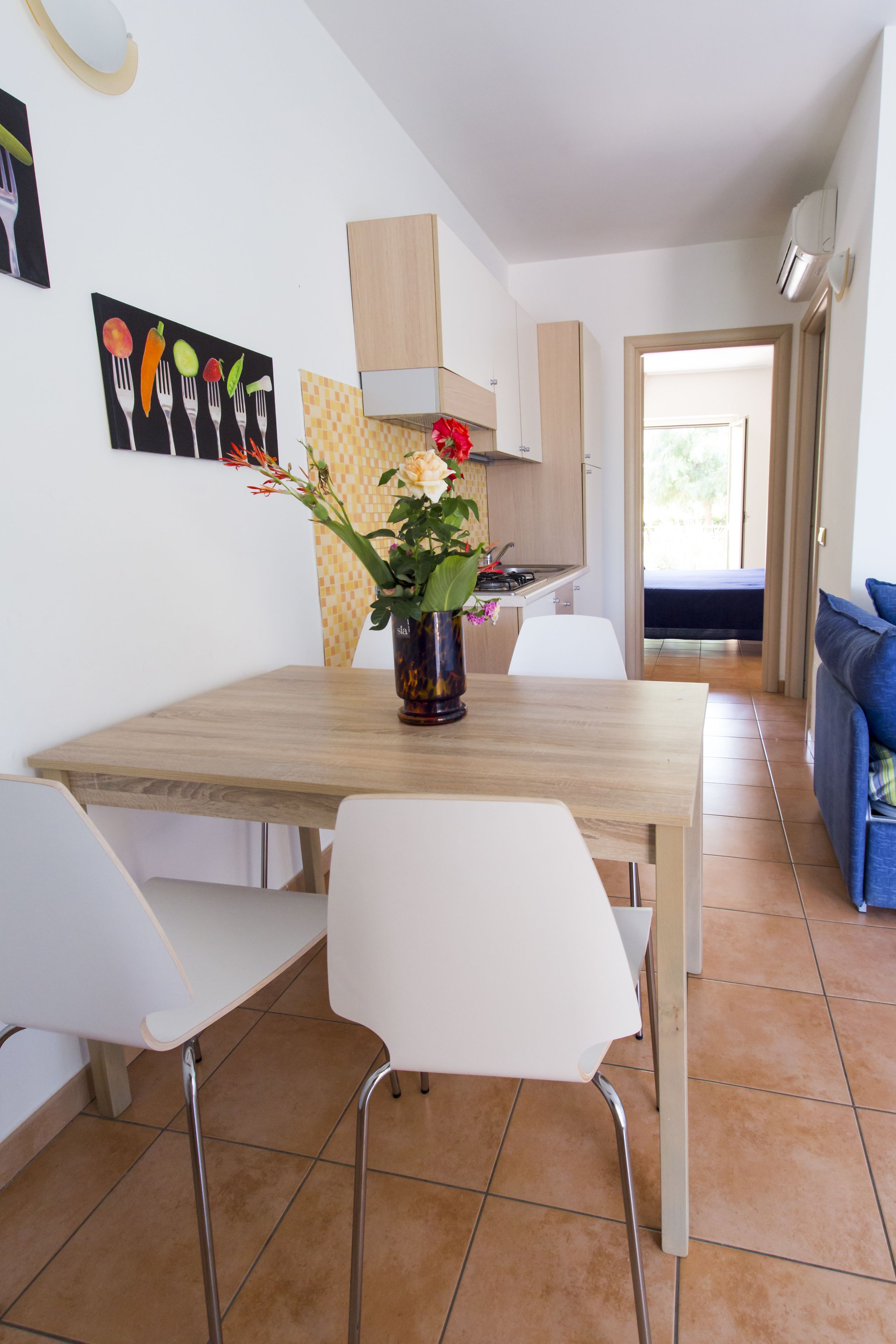 Ein Essbereich mit einem Holztisch, weißen Stühlen, einer Blumenvase und Wandbildern.