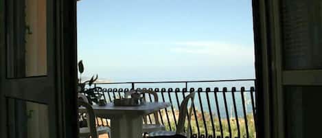A balcony with a table and chairs, overlooking a coastal landscape.