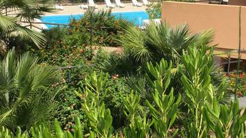 A pool area with lounge chairs and umbrellas, surrounded by lush greenery and flowering plants.