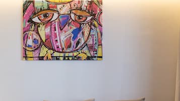 A wooden sofa with grey cushions against a white wall, with a colorful abstract painting above it.