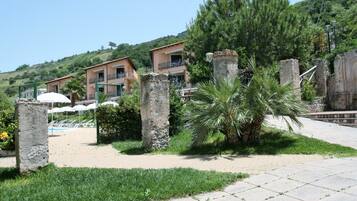 A courtyard with stone pillars, a palm tree, and a pool area with umbrellas.