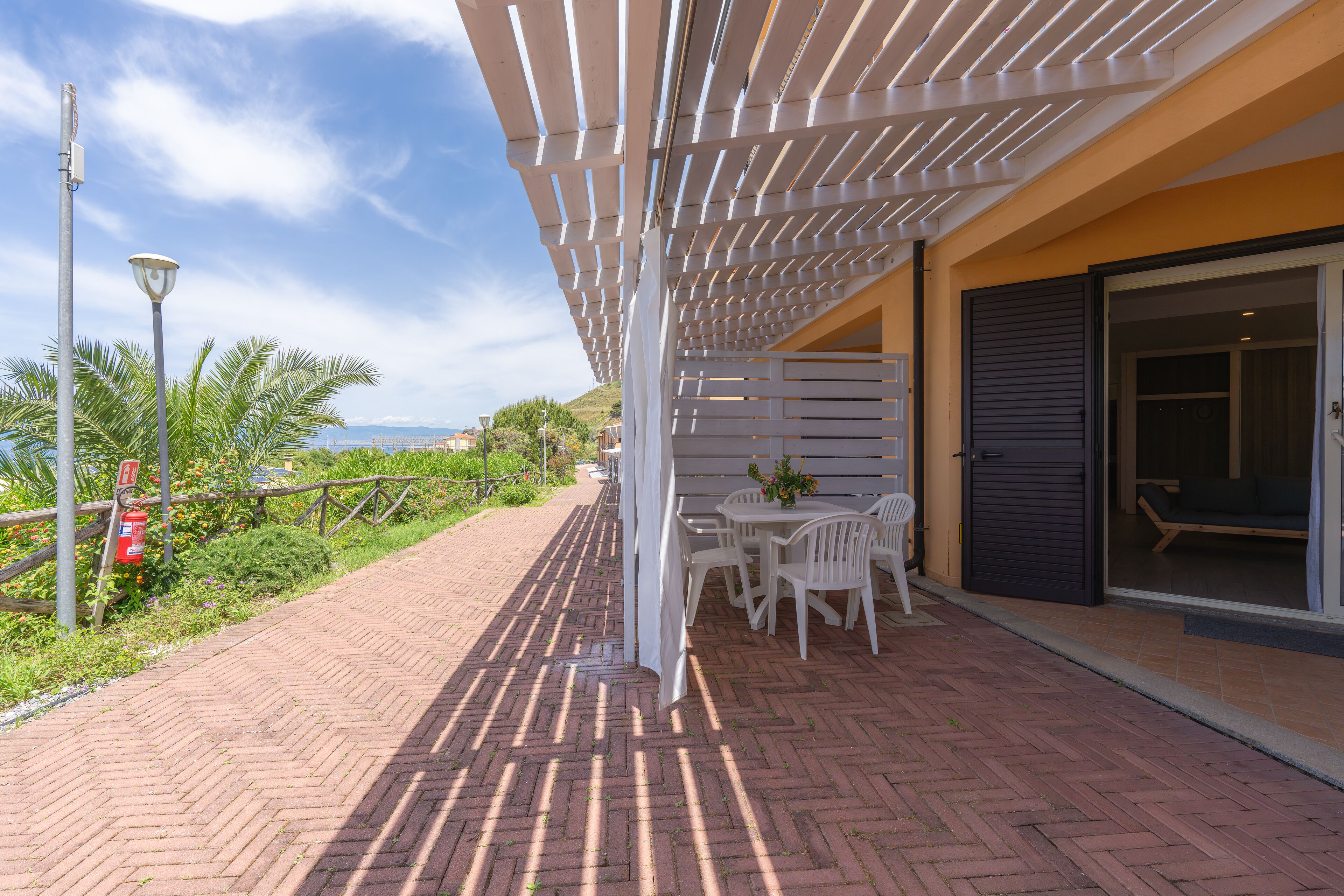 An outdoor patio with a white pergola, brick flooring, and a table with chairs.