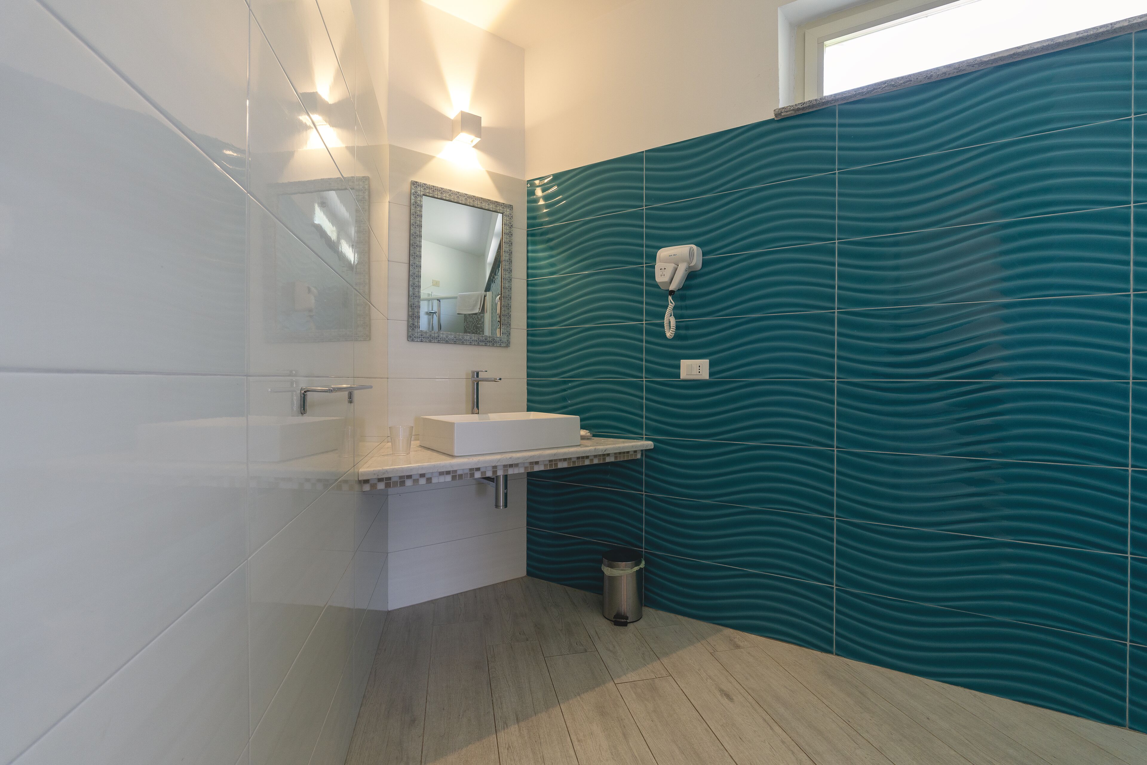 A modern bathroom with a white sink, a mirror, and a hairdryer mounted on the wall.