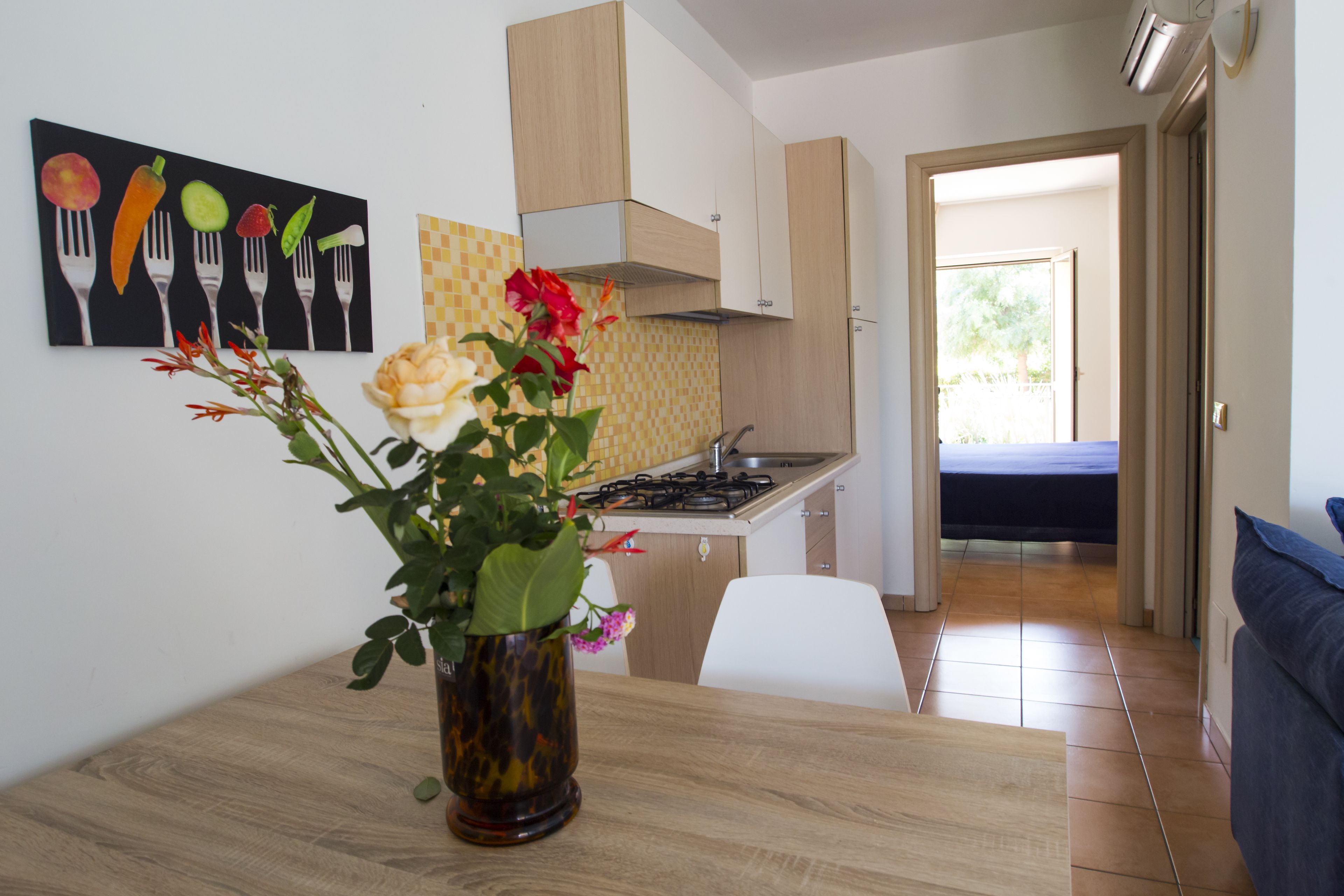 Eine moderne Küche mit Esstisch, Blumen in einer Vase und einem Bild von Kochutensilien an der Wand.