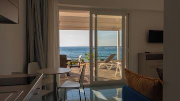 A room with a view of the sea, a dining area, and a TV on the wall.