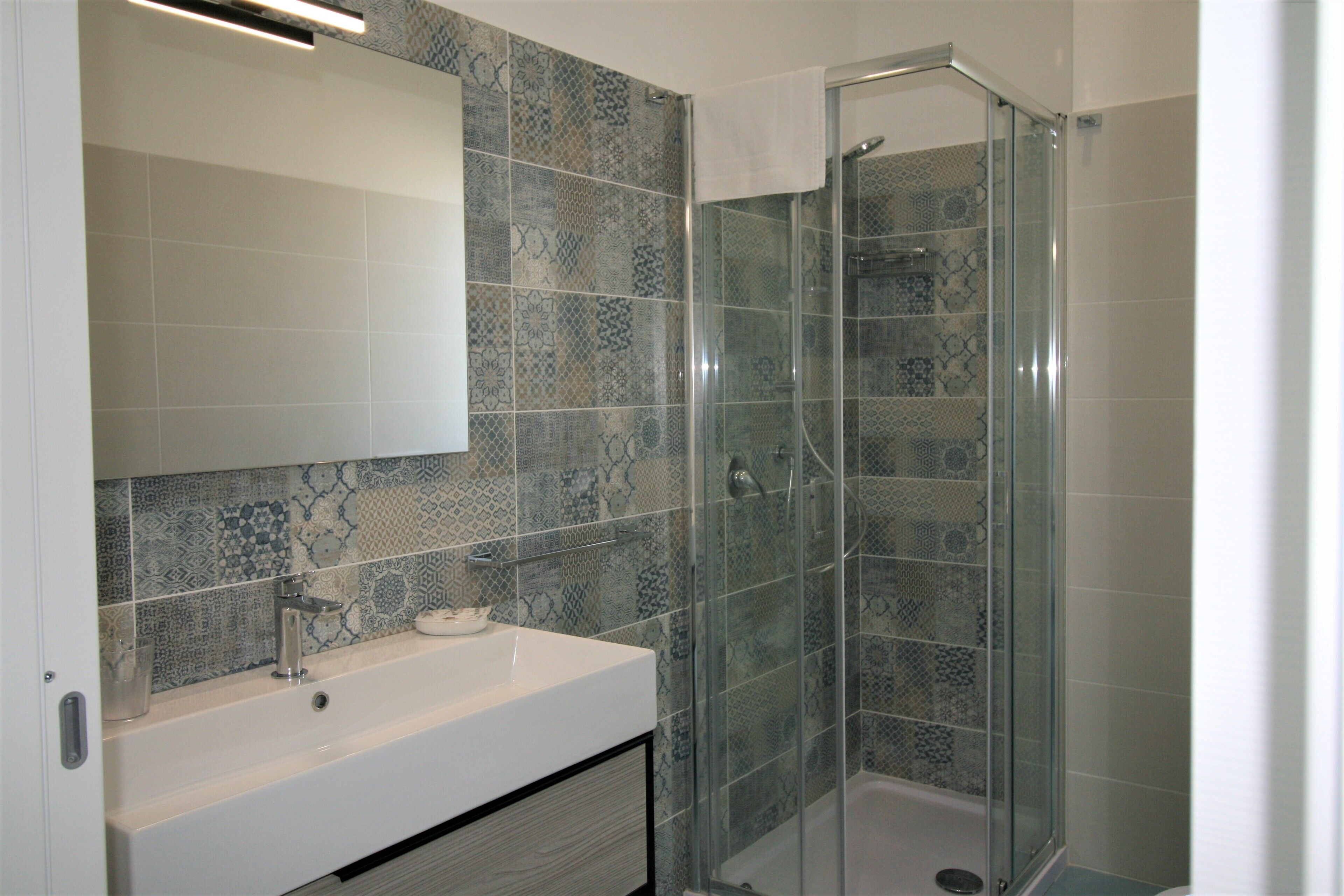 A bathroom with a glass-enclosed shower, a white sink, and patterned tiles.