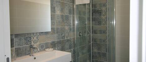 A bathroom with a glass-enclosed shower, a white sink, and patterned tiles.