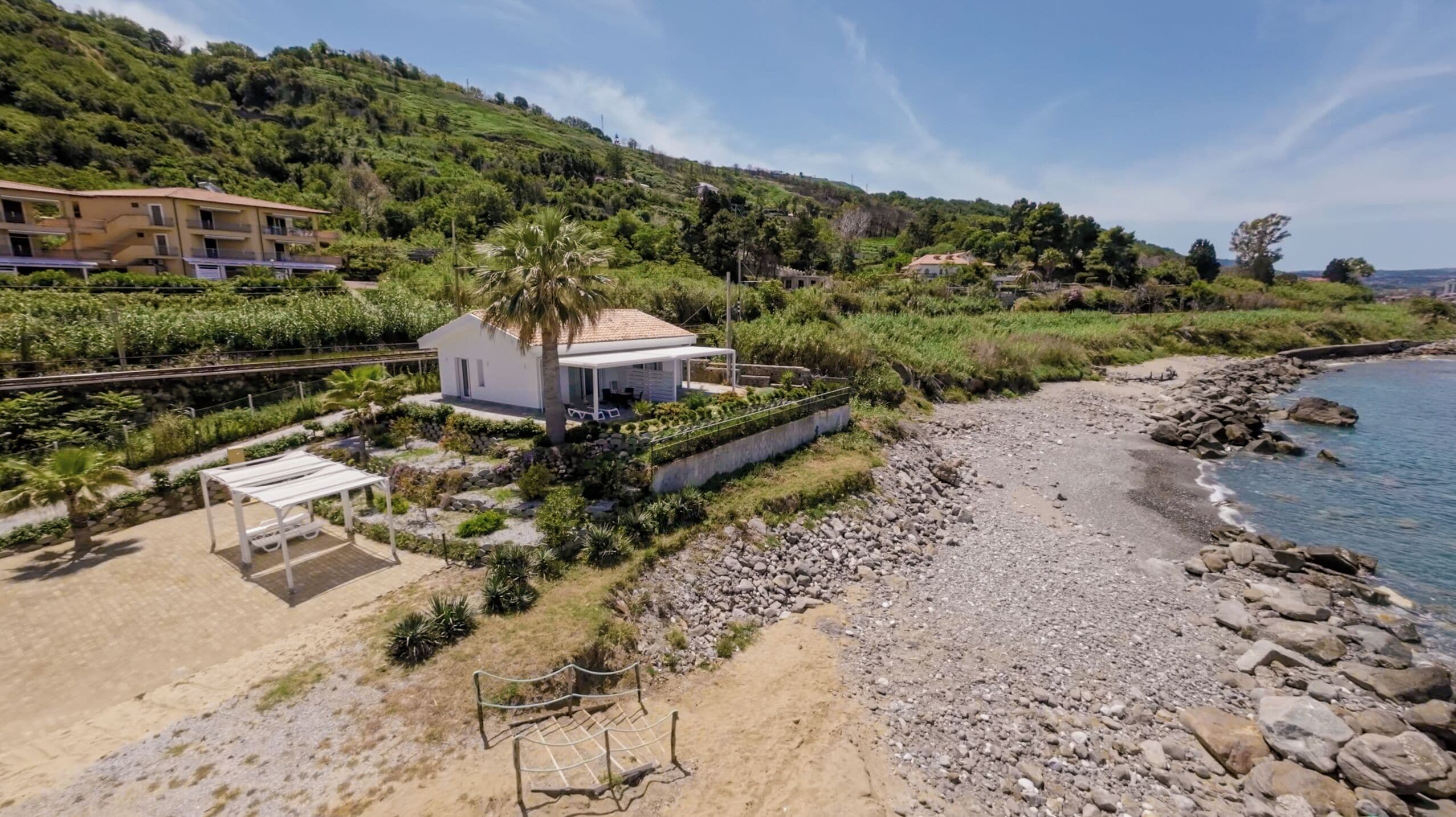 Een kustpand met een wit huis, een overdekte patio en een rotsachtig strand.