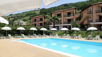 Una piscina con sillones de descanso y sombrillas, rodeada de edificios de varios pisos con balcones.