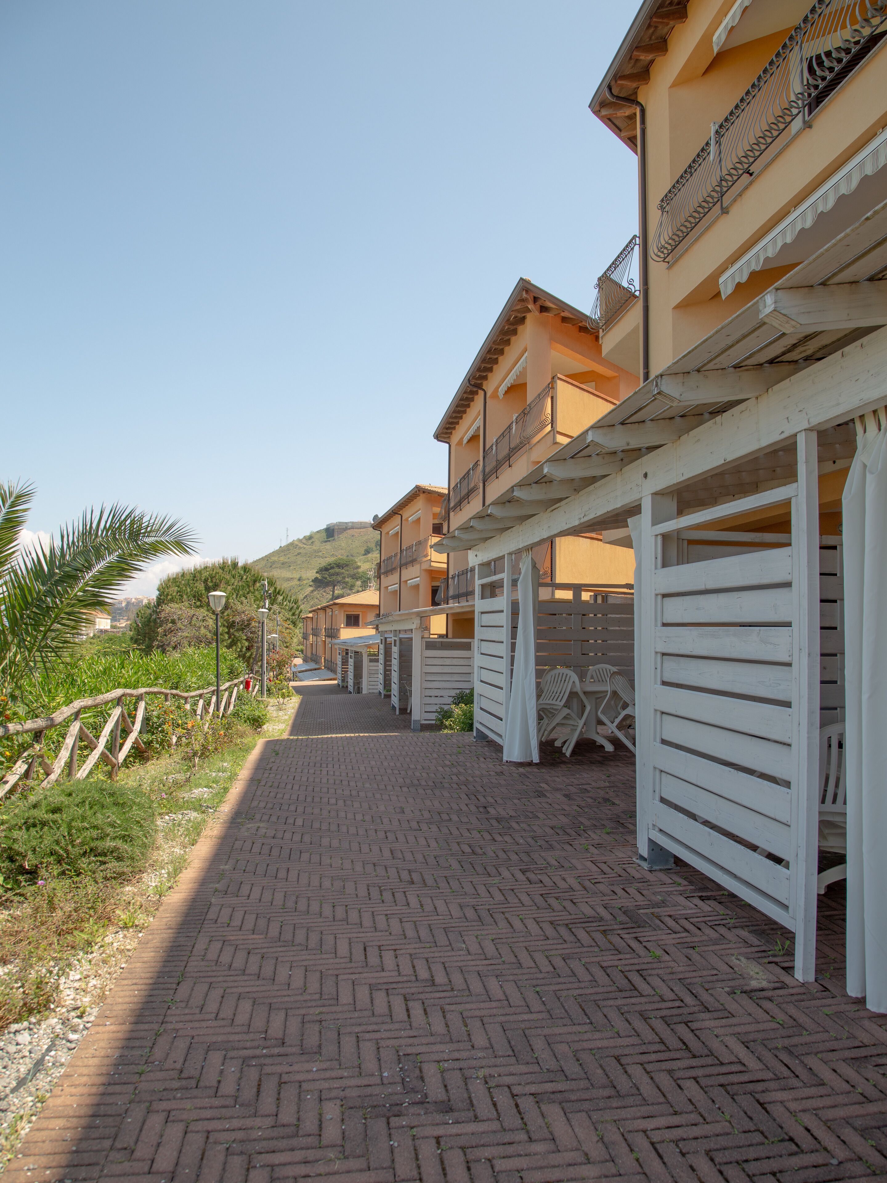 A row of seaside buildings with balconies, a brick pathway, and a wooden fence.