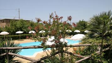 A swimming pool with white umbrellas, surrounded by greenery and a wooden fence.