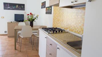 Une cuisine compacte équipée d’une cuisinière à gaz, d’un évier et d’un coin repas avec des chaises.