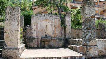 Ruinas antiguas con columnas de piedra y escalones, rodeadas de vegetación y un edificio al fondo.