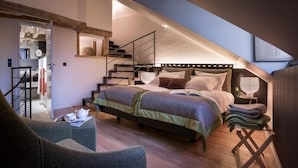 Une chambre avec un plafond en pente, un lit doté d’une tête de lit, un escalier et un petit coin salon.