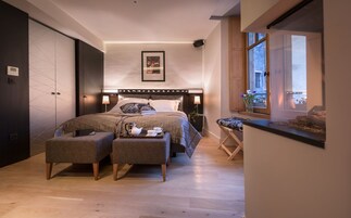 A modern bedroom with a large bed, bedside tables, a small seating area, and a window with a view.