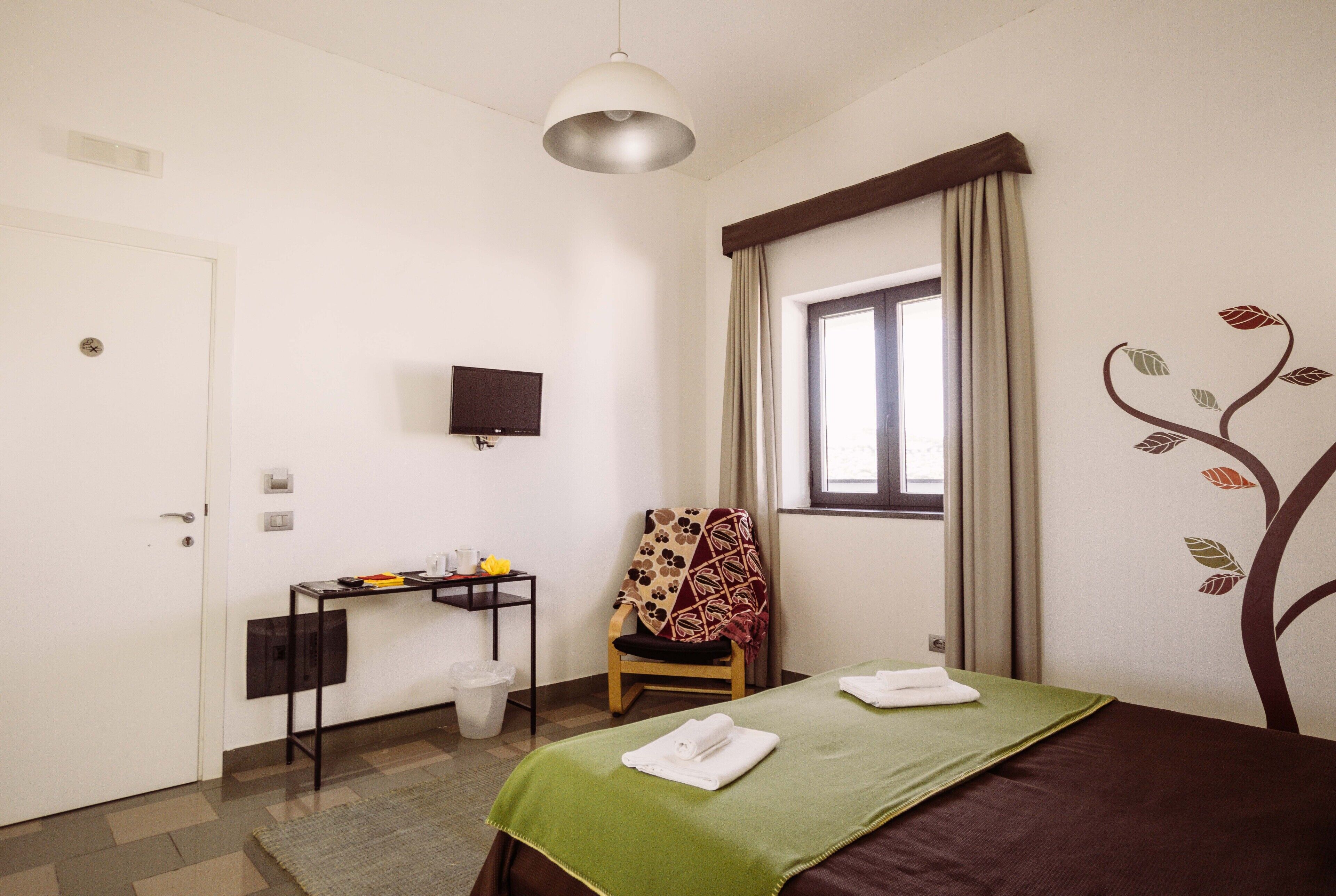A hotel room with a bed, a desk, a chair, a television, and a window with curtains.