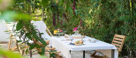 An outdoor dining area with a table set for a meal, surrounded by greenery and plants.