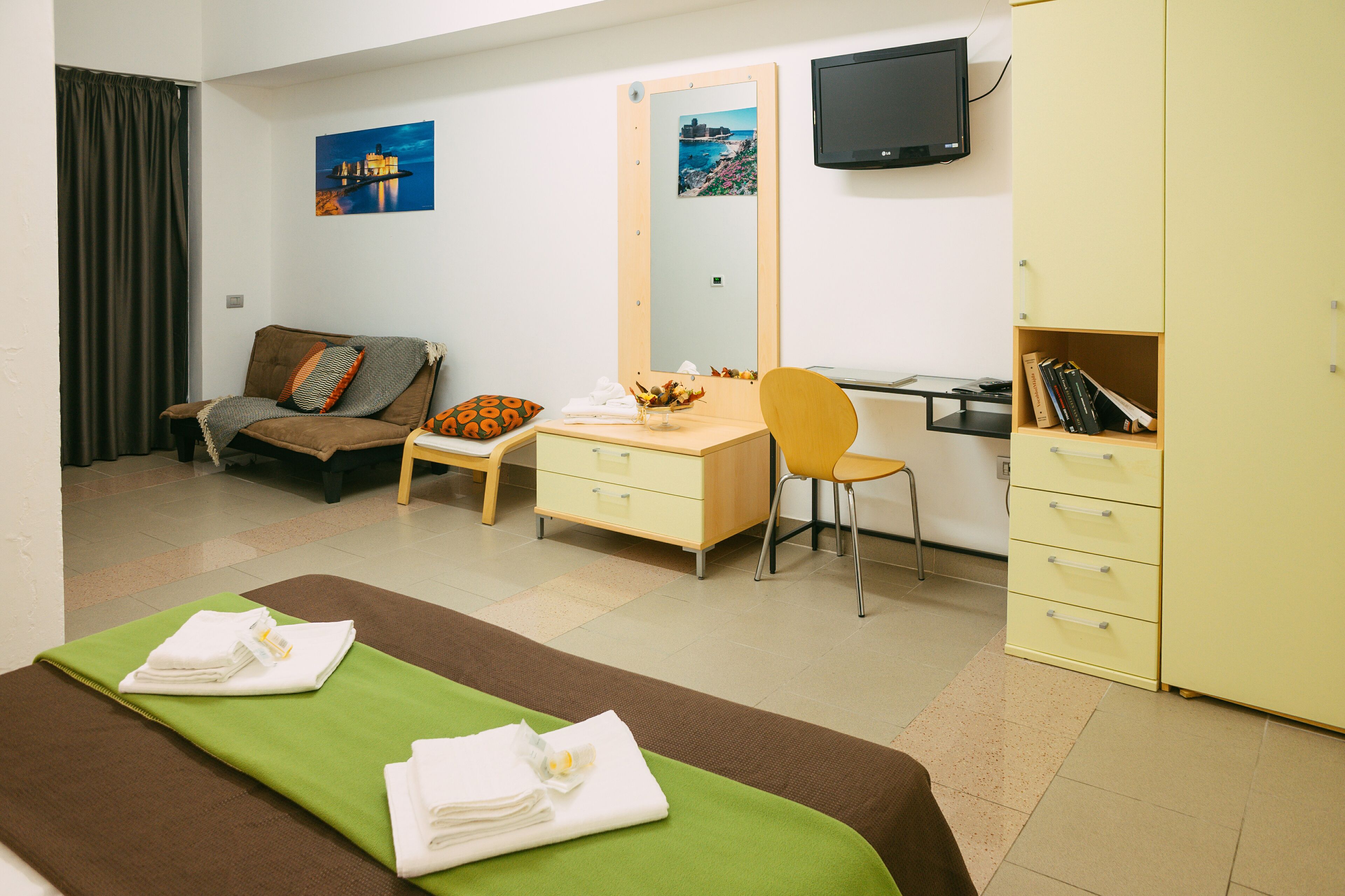 Ein Hotelzimmer mit Bett, Schreibtisch, Sessel, Fernseher und Kleiderschrank.