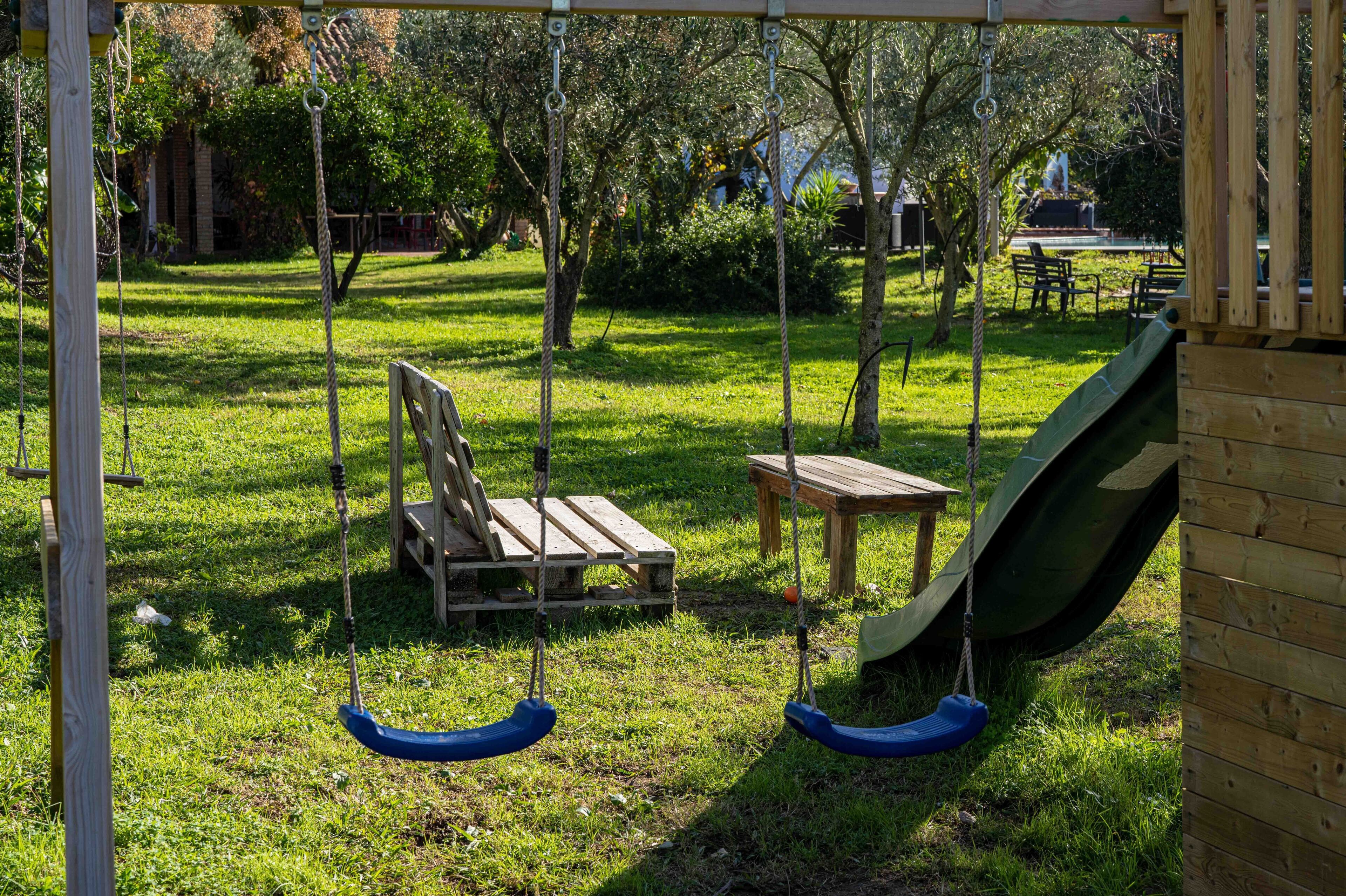 A wooden swing set with two swings and a small table in a grassy park area.