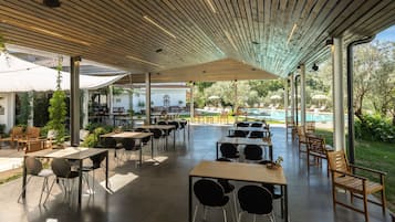 Un patio al aire libre con mesas y sillas, una piscina al fondo y un área de estar techada con sombrillas.