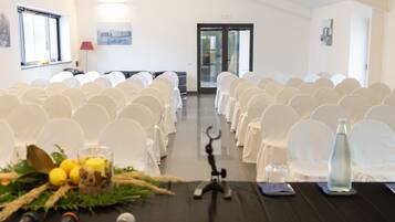 Ein Konferenzraum mit Reihen weißer Stühle, einem schwarzen Tisch mit Mikrofonen und einer Glasflasche auf dem Tisch.