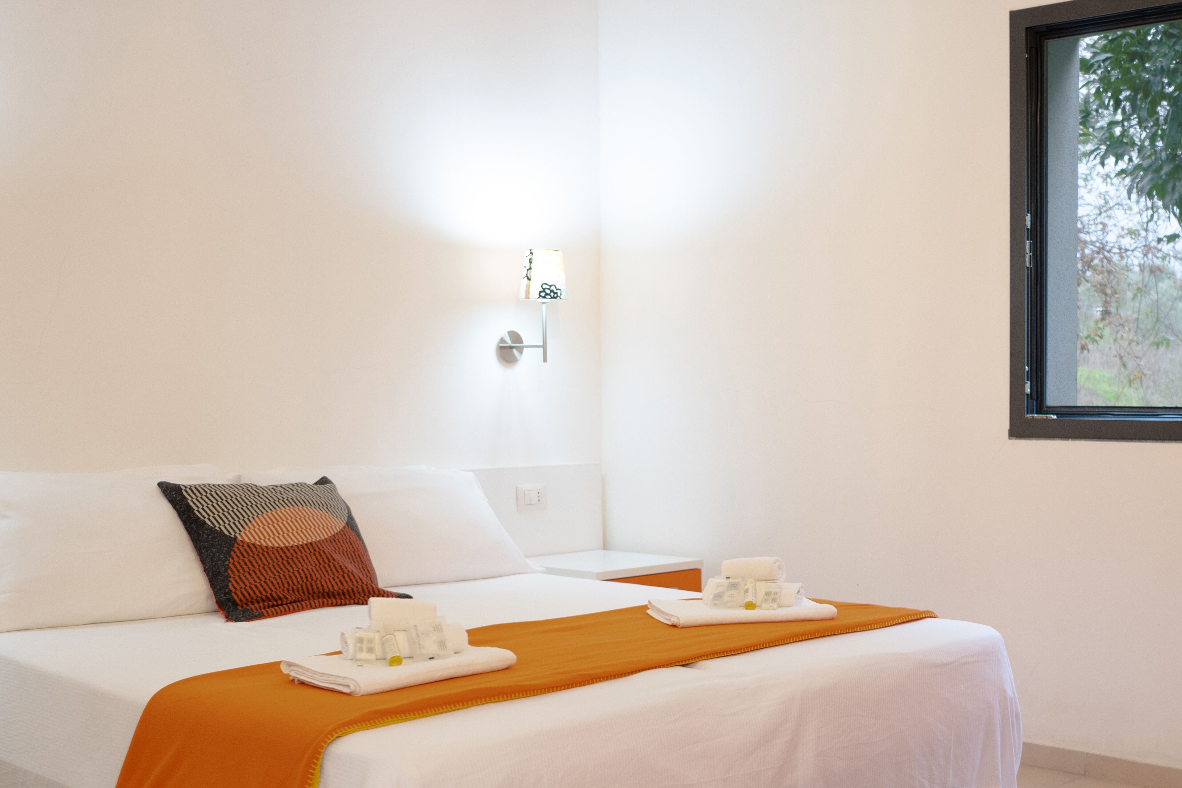 A hotel room with a bed, a nightstand, a lamp, and a window.
