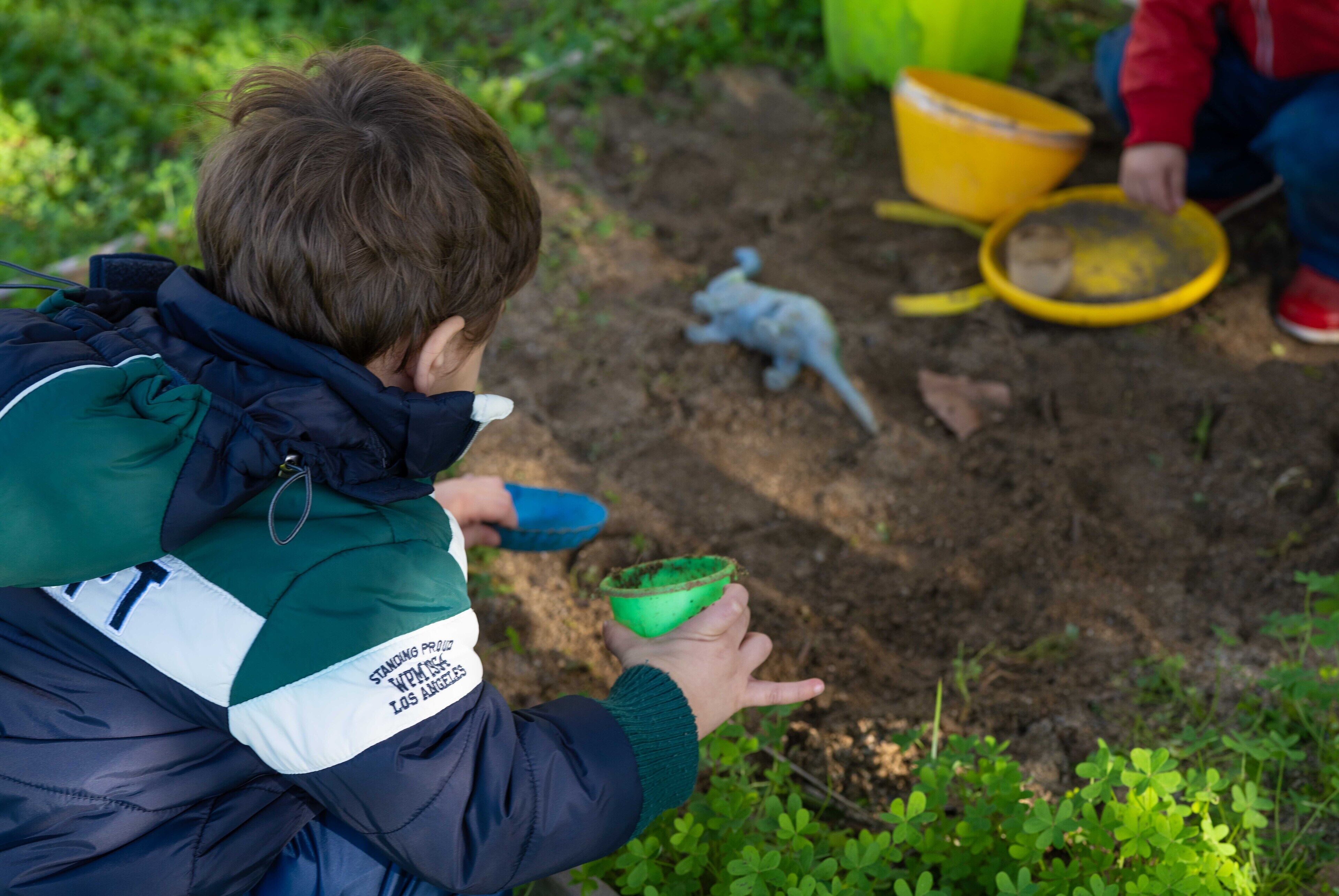 A child holding a green container, with a dinosaur toy and a yellow bucket in the background.