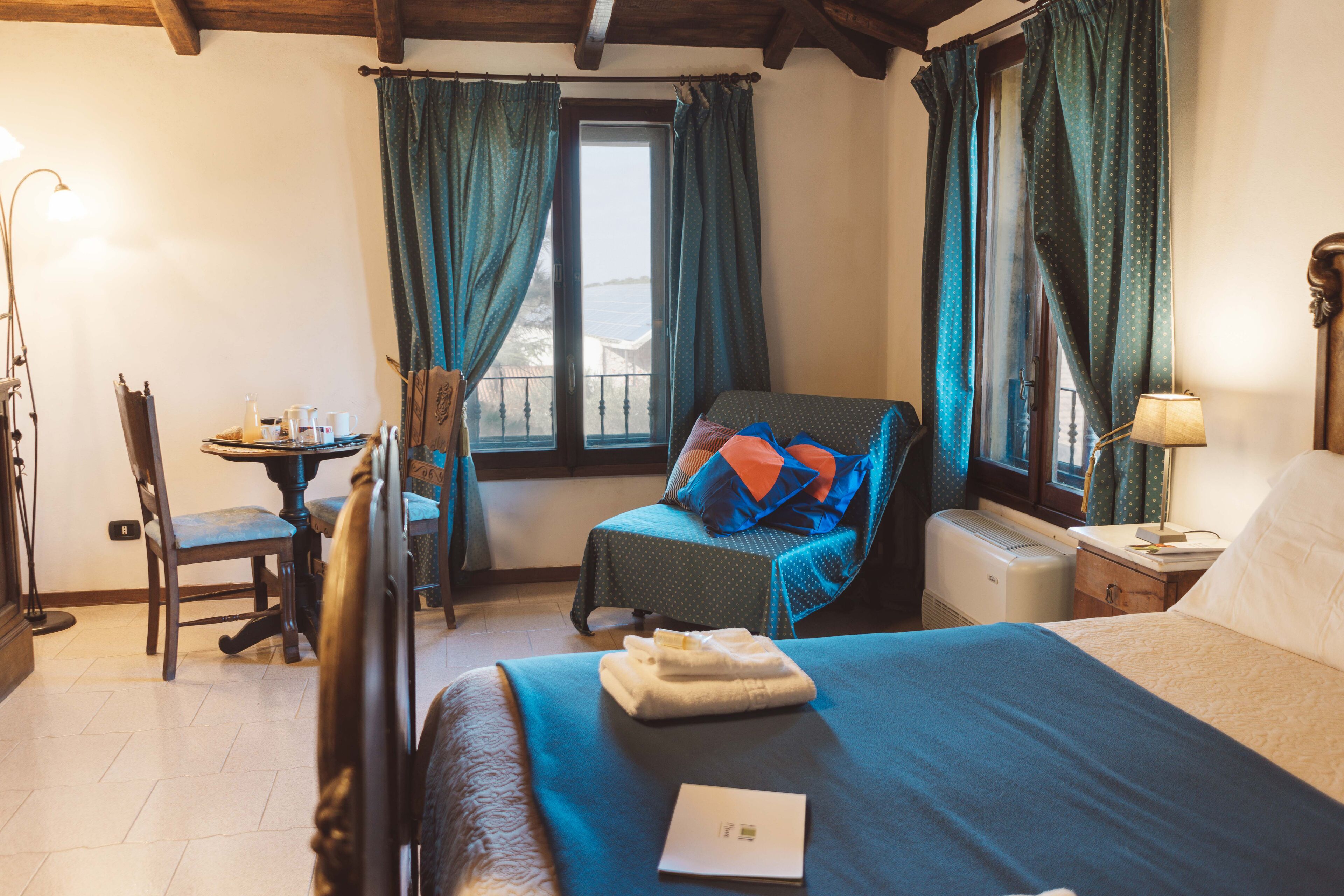 A bedroom with a bed, a chair, a table with a lamp, and a window with curtains.
