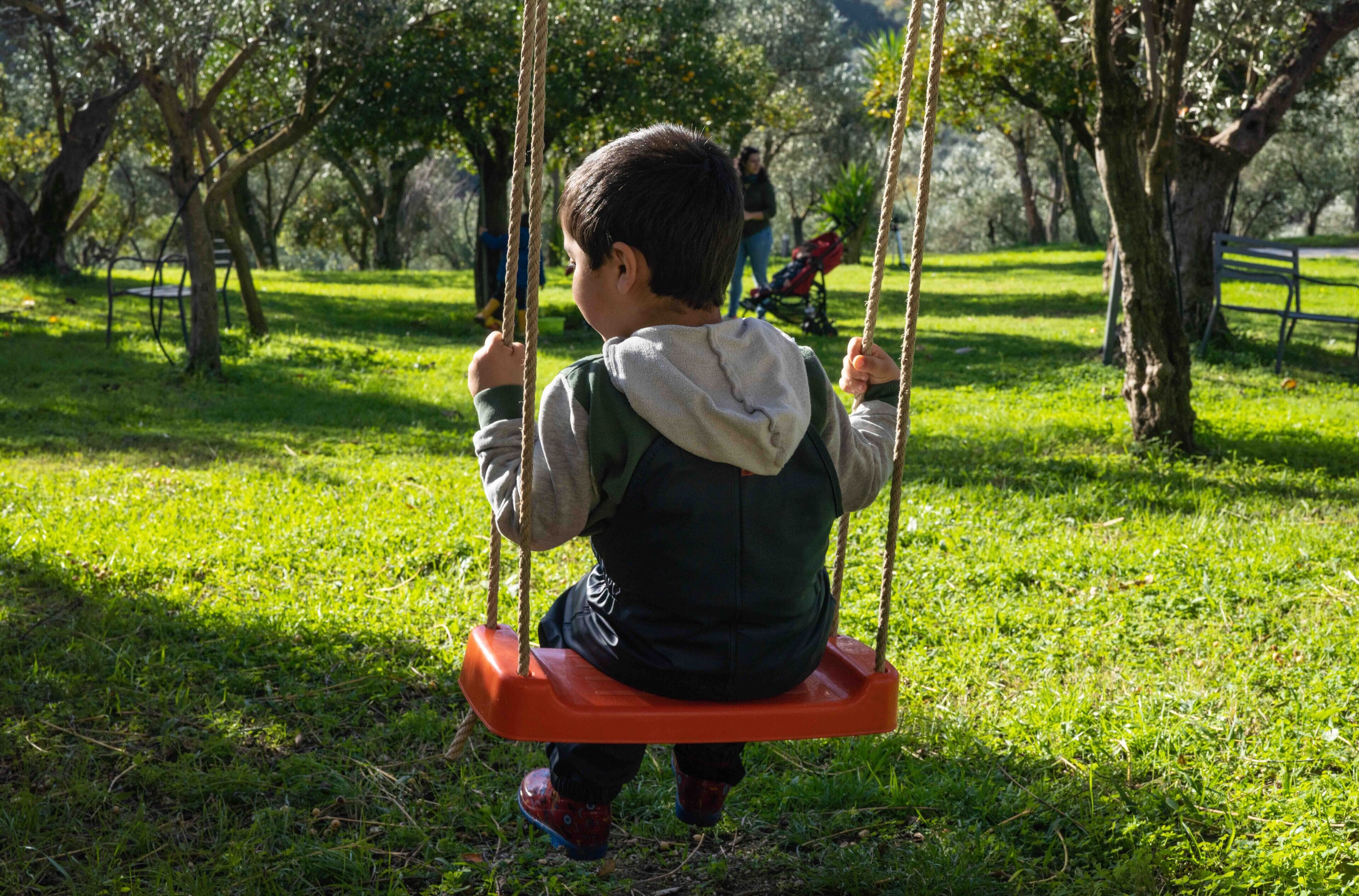 Uma criança num baloiço em um parque com relva e árvores.
