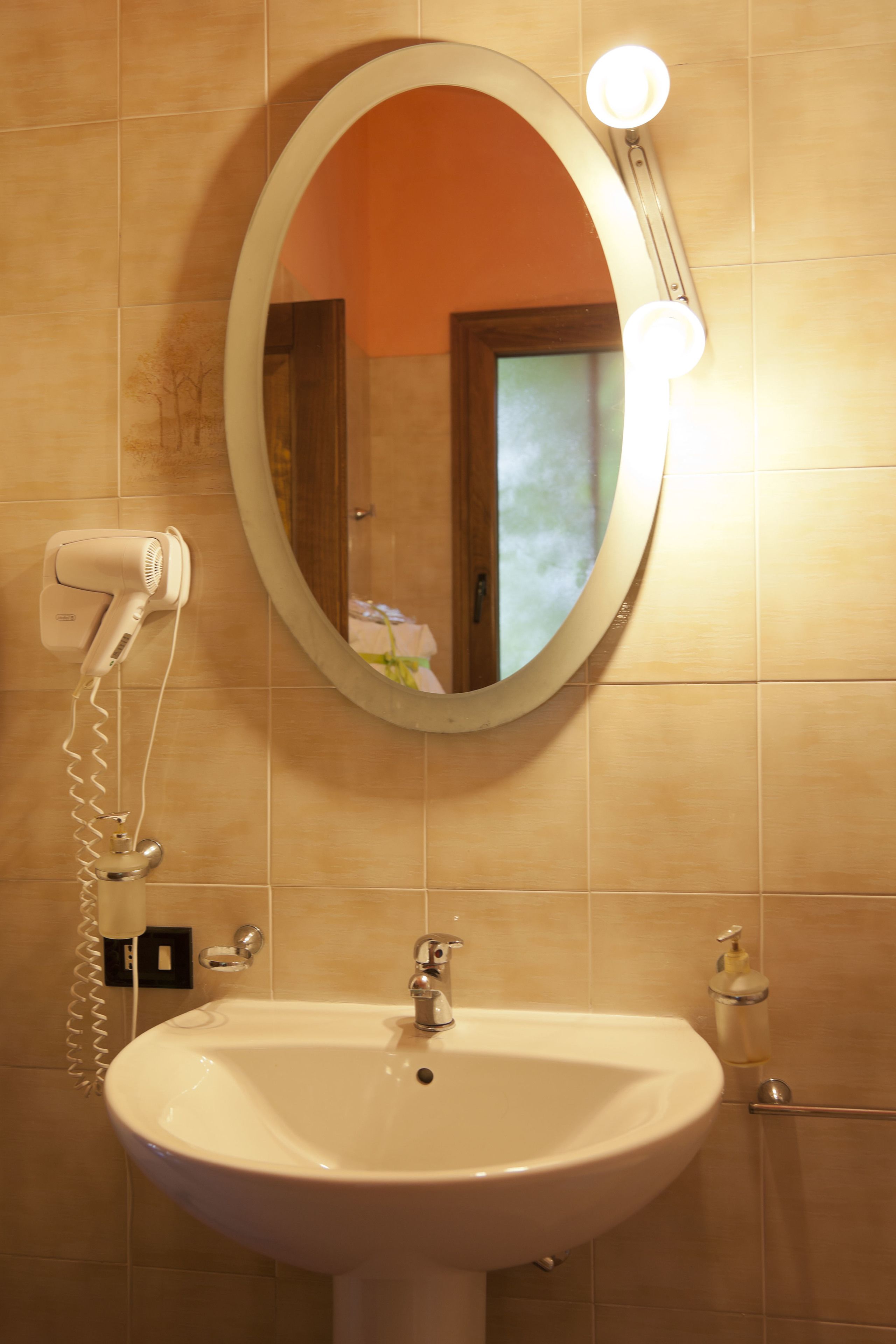 A bathroom with a white sink, a mirror, and a hairdryer on the wall.