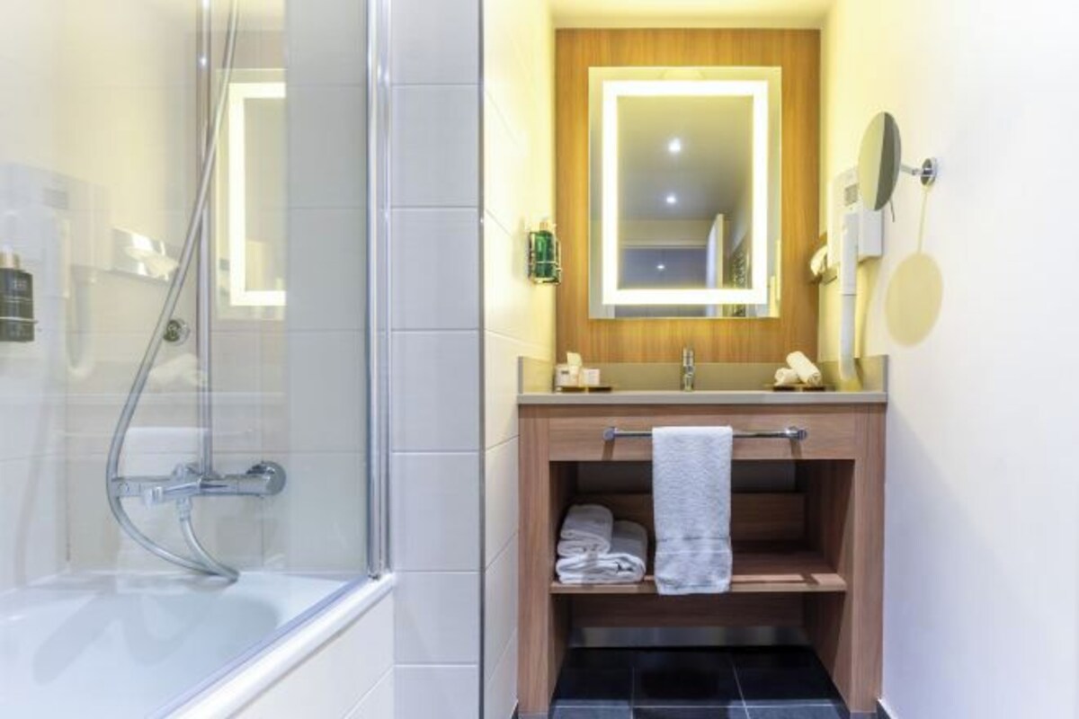 Een badkamer met een douche in een glazen cabine, een houten wastafelmeubel met spiegel en een handdoekrek.