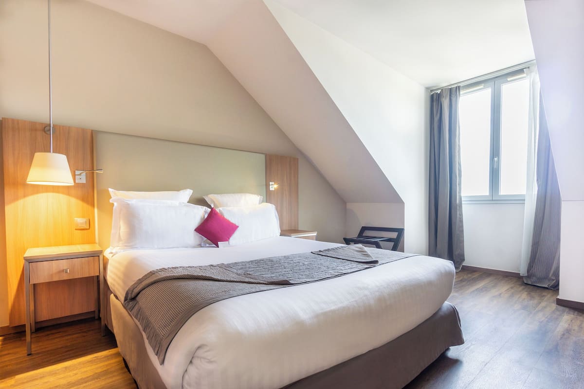 Une chambre d’hôtel moderne avec un grand lit, une table de chevet, une lampe et une fenêtre avec des rideaux.