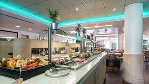 Ein Buffetbereich mit verschiedenen Früchten und Gemüsesorten, einer Selbstbedienungsstation und einer Sitzgelegenheit mit Tischen und Stühlen.