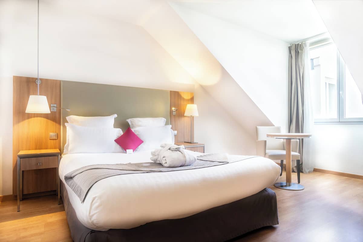 Une chambre d’hôtel moderne avec un grand lit, une table de chevet, une petite table et une lampe.