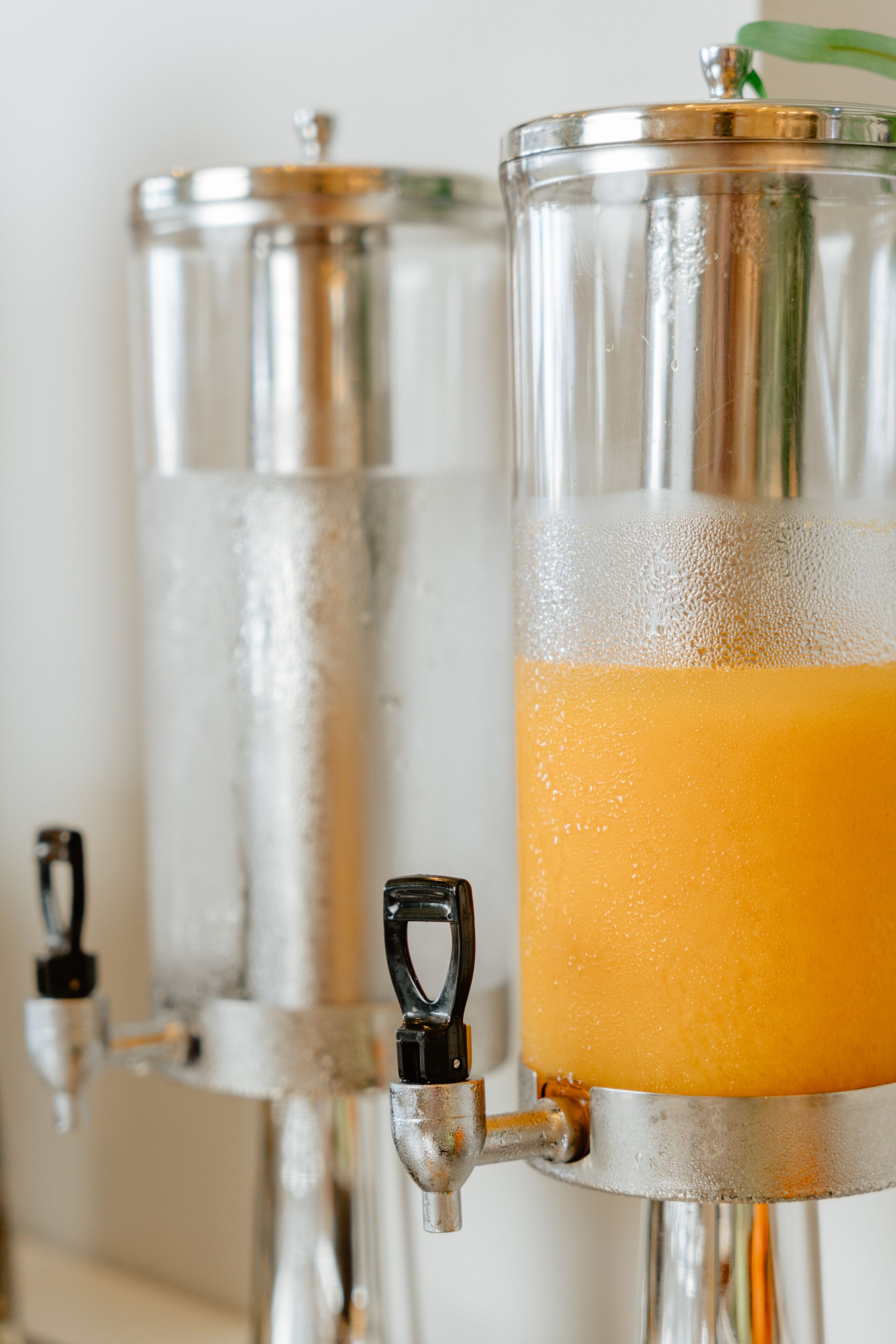 A beverage dispenser with a clear glass container filled with orange juice.