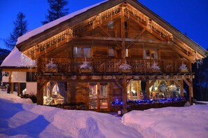 Una cabaña de madera con balcón, techo nevado y luces colgantes.